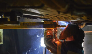 A mechanic working underneath a vehicle while sparks flies off the welding tool.