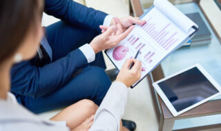 High angle closeup of two business people pointing at statistics graph with marketing and financial data discussing project development during meeting in modern office