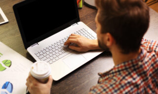 Enjoying good working day. Confident young man working on laptop while sitting at his working place