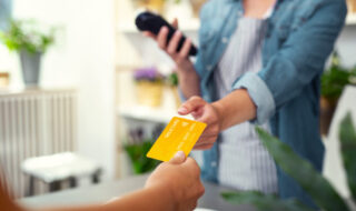 A female handing over a yellow cedit card to another female while on the phone and outdoors