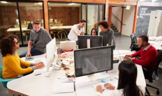 Casually Dressed Business Team Working At Desks In Modern Open Plan Office