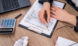 Writing on a clipboard with a crumpled piece of paper and glasses nest to it.