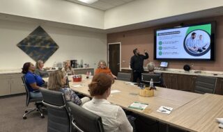 An office meeting about helath realted topics being displayed on a flastscreen TV.