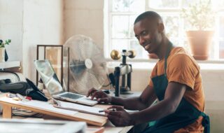 African small business owner smiling with paperwork and laptop