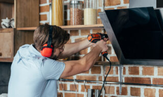 young man in earmuffs drilling kitchen hood with electric drill