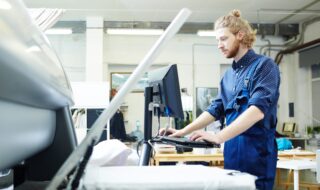 Man with a beard standing at a printer wearing a blue shirt.