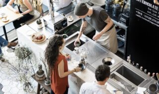 Three people at a coffee bar, and one behind the counter is preparing a drink for the others.