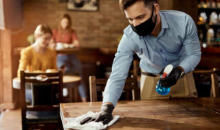 Waiter wearing face mask cleans table coronavirus covid