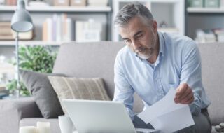 Man using a laptop while holding a piece of paper