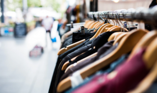 Clothes on a rack with hangers on the street during the daytime and a blurry image of a person in the background